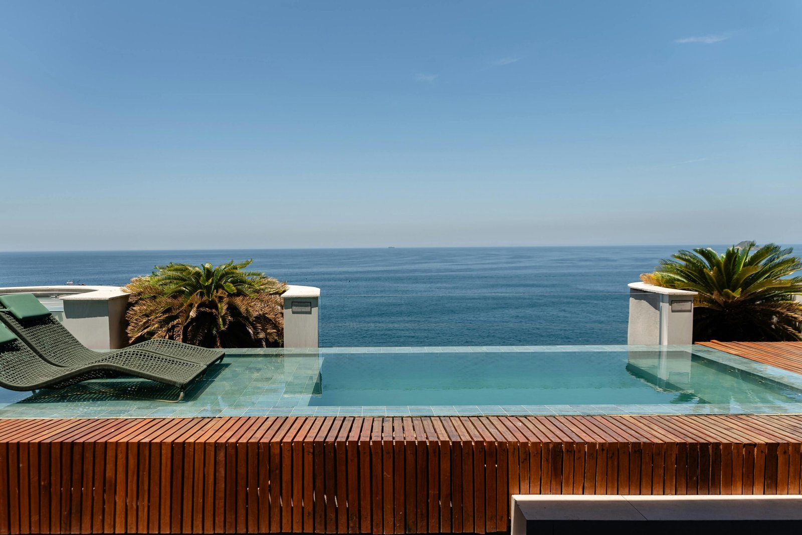 Elegant infinity pool with ocean view at a luxury resort, featuring sleek lounge chairs and tropical plants.